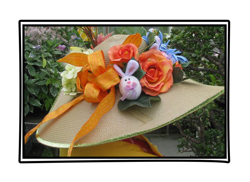 An Easter Bonnet hat with rabbits, flowers, and orange ribbon attached to the rim. The hat is on somebody's head